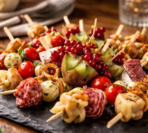 KI generiert: Vielfältige Antipasti-Spieße mit Kiwis, Tomaten, Käse und Salami auf einer Schieferplatte.