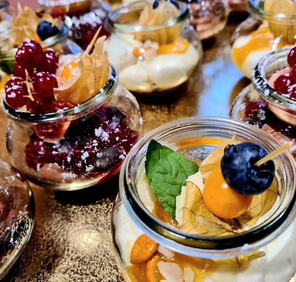 KI generiert: Das Bild zeigt eine Auswahl von Desserts in kleinen Gläsern, die mit verschiedenen Früchten wie Johannisbeeren, Physalis und Blaubeeren garniert sind. Die Desserts haben bunte Toppings und wirken sehr dekorativ und appetitlich.