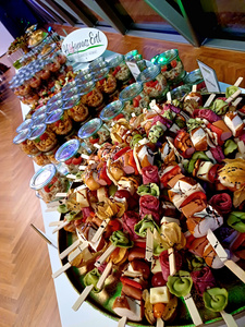 KI generiert: Das Bild zeigt eine Auswahl an bunten Fingerfood-Spießen und Gläsern mit Vorspeisen, die dekorativ auf einem Tisch präsentiert werden. Der Hauptinhalt des Bildes ist ein ansprechend angerichtetes Buffet mit einer Vielzahl an Appetithäppchen.