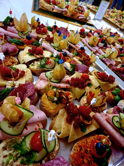 KI generiert: Bunte, dekorative Häppchen mit Aufschnitt, Gemüse und Obst auf einem Buffet.