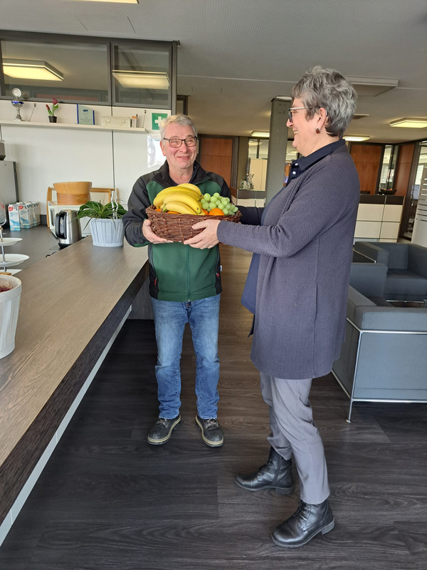 KI generiert: Zwei Personen tauschen einen Obstkorb in einem modernen Raum aus.