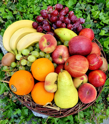 KI generiert: Korb mit verschiedenen Früchten: Bananen, Trauben, Äpfel, Orangen, Birnen, umgeben von Efeu.