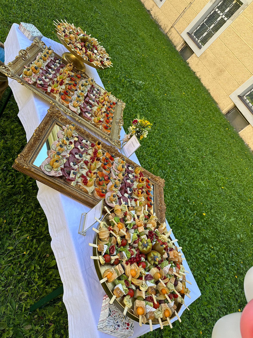 KI generiert: Ein Buffet mit belegten Brötchen und Obstspießen auf dekorativen Tabletts im Freien.