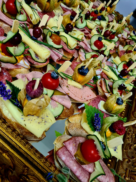 KI generiert: Das Bild zeigt eine Vielzahl von kunstvoll angerichteten Canapés, die mit verschiedenen Zutaten wie Käse, Wurst, Gemüse und Beeren dekoriert sind. Die Canapés sind auf einem dekorativen Tablett arrangiert.